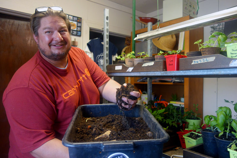 Brian Fraus, owner of Texas Big Worm Farm in Bertram, holds a bin of compost, complete with coffee grounds and filters, that he uses to nourish seedlings for his garden, some of which brighten up his office on a cloudy March afternoon. Staff photo by Suzanne Freeman