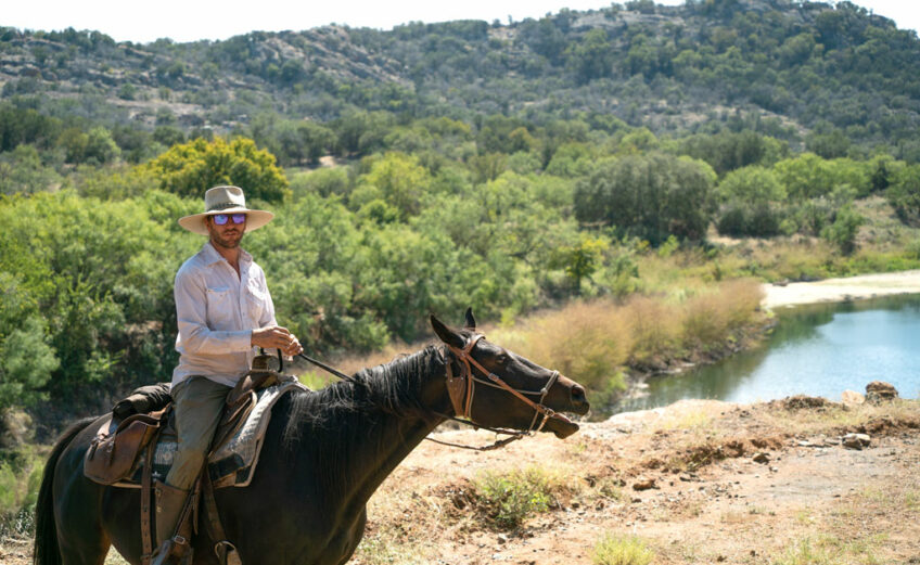 Travis Caffee with his horse Ria in front of a flooded quarry used for scuba diving on Reveille Peak Ranch in Burnet County. Ria is one of 12 horses that Caffee trained for trail rides and riding lessons through his Thunder Horse Outfitters. Staff photo by Dakota Morrissiey